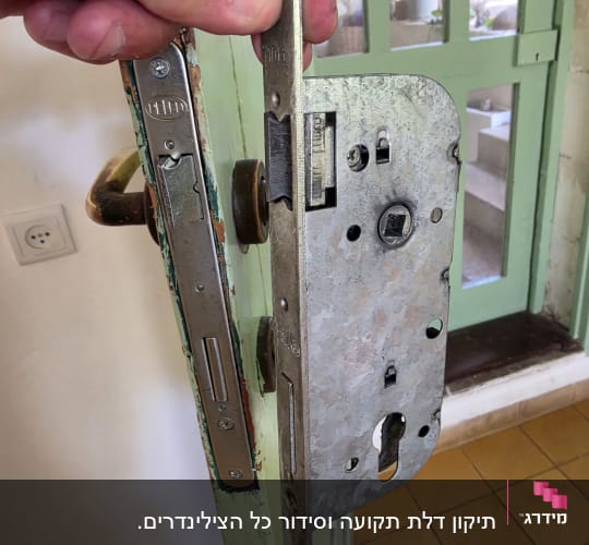 מנעול דלת ישן מוחזק ביד ליד דלת ירוקה